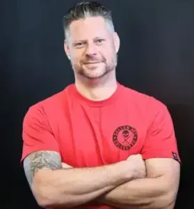 Man with crossed arms in a red T-shirt against a dark background