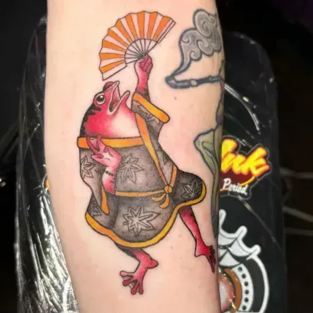 Colorful frog tattoo with umbrella, smoke, and gray robe on a person's arm