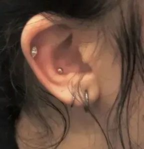 Close-up of an ear with multiple piercings and loose dark hair framing it
