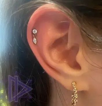 Close-up of an ear with a small gold dangling earring and two tiny upper ear piercings.