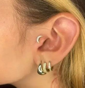 Close-up of an ear with a small crescent stud and three gold hoop earrings