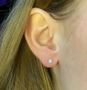 Close-up of an ear with a small silver stud earring and light brown hair nearby