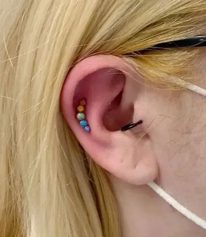 Close-up of an ear with colorful bead piercings and a black ear cuff.