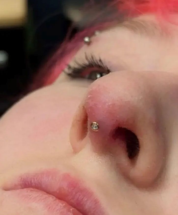 Close-up of a nose with a silver nose stud and pink hair visible near the eye.