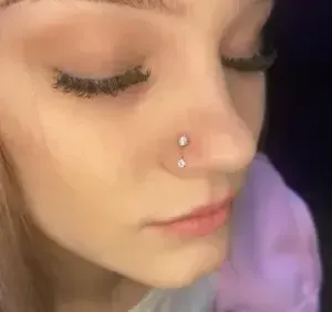Close-up of a face with closed eyes and a silver nose stud, softly lit against a dark background