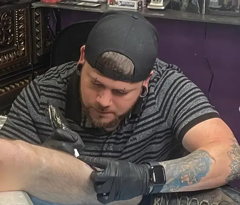 Tattoo artist in black gloves working at a station, looking down in concentration.