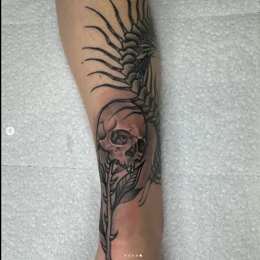 Forearm tattoo of a skull with a sunburst or spider-like design above it