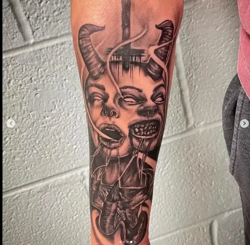 Black-and-gray tattoo of a surreal horned face on a person’s lower leg