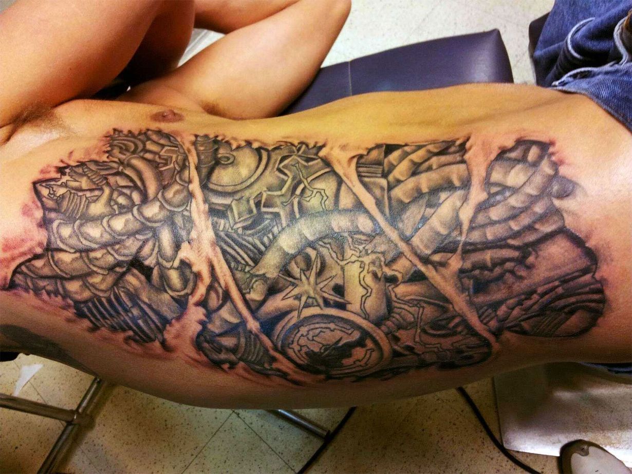 Large black-and-gray tattoo covering a person’s forearm, showing an intricate cross and geometric design.