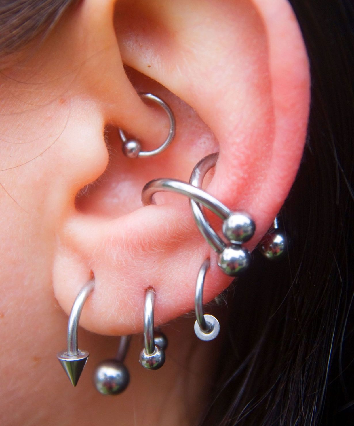 Close-up of an ear with multiple silver piercings and dangling studs