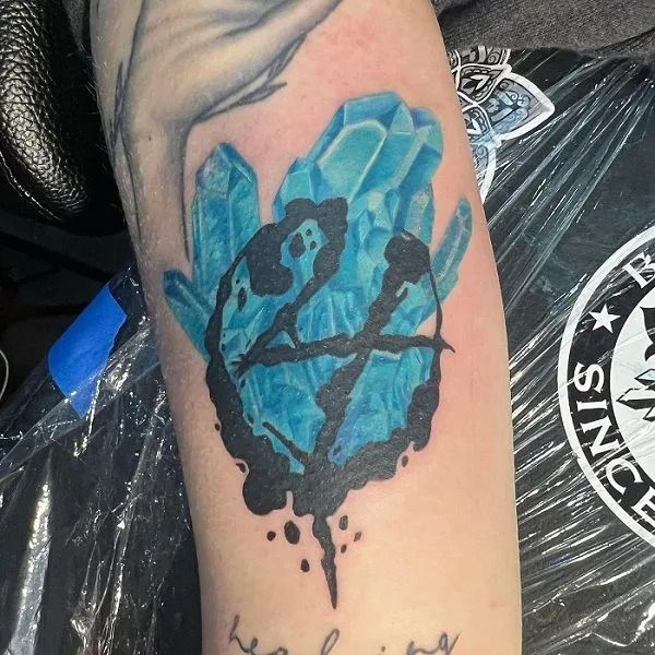 Blue crystal tattoo on a forearm with a dark silhouette design and ink drips