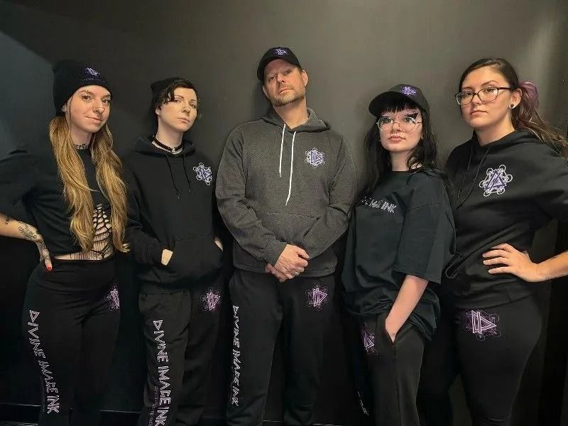 Five people in black and gray matching athletic outfits pose against a plain backdrop.
