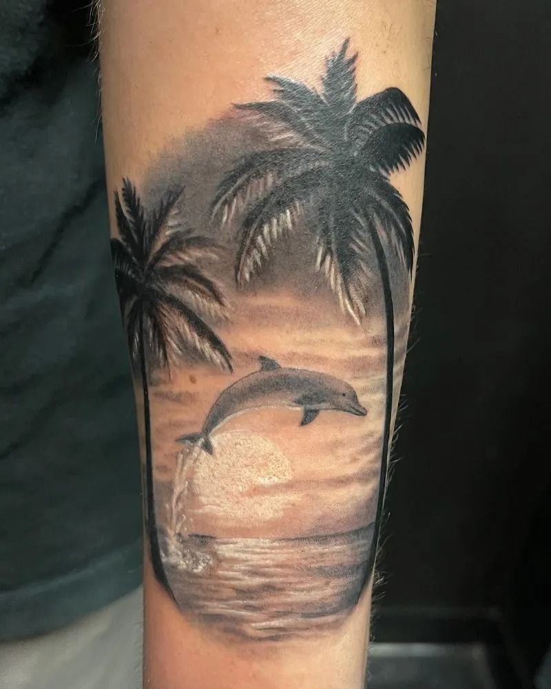 Black-and-gray wrist tattoo of a tropical sunset with palm trees, dolphin, and ocean waves