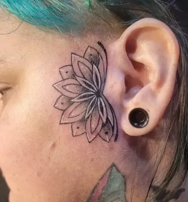 Close-up of a face with a floral tattoo near the eye and a black ear gauge.