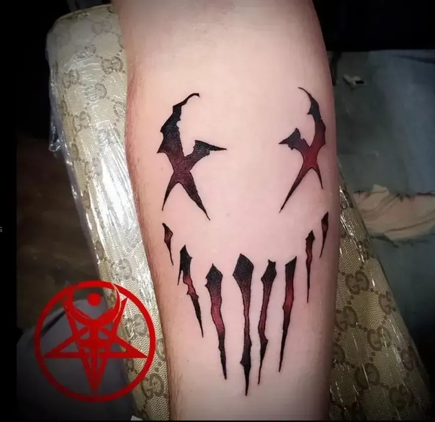Close-up of a forearm with a black-red horror-style tattoo design and a red pentagram symbol.