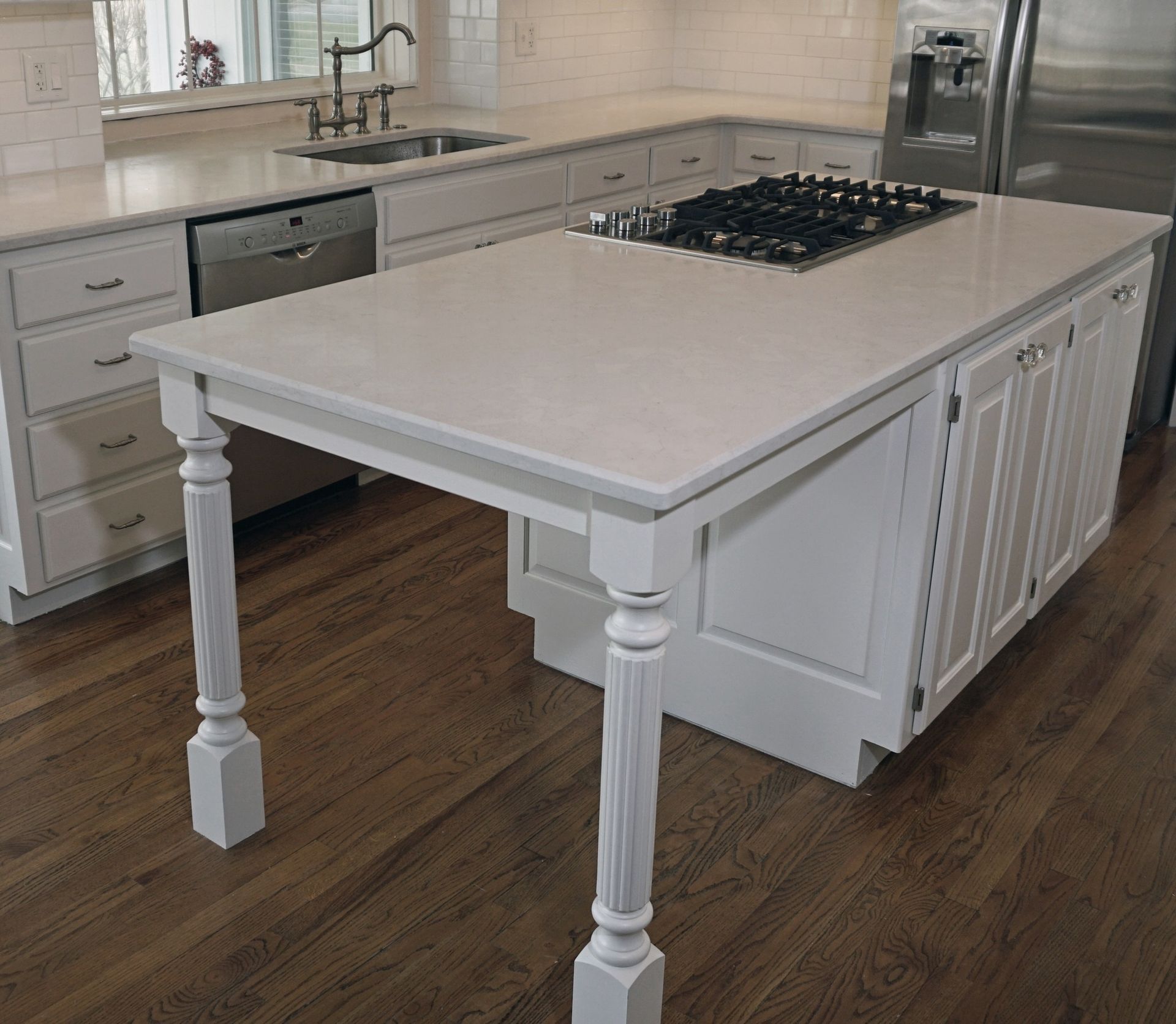 A kitchen with white cabinets and a large island with a stove top oven