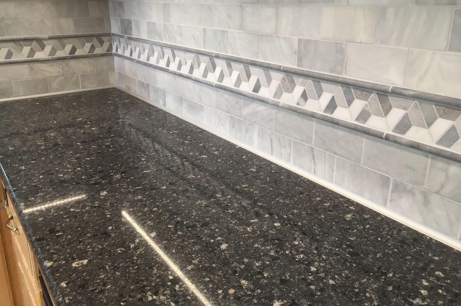 A kitchen counter with a black granite counter top and a gray tile border.