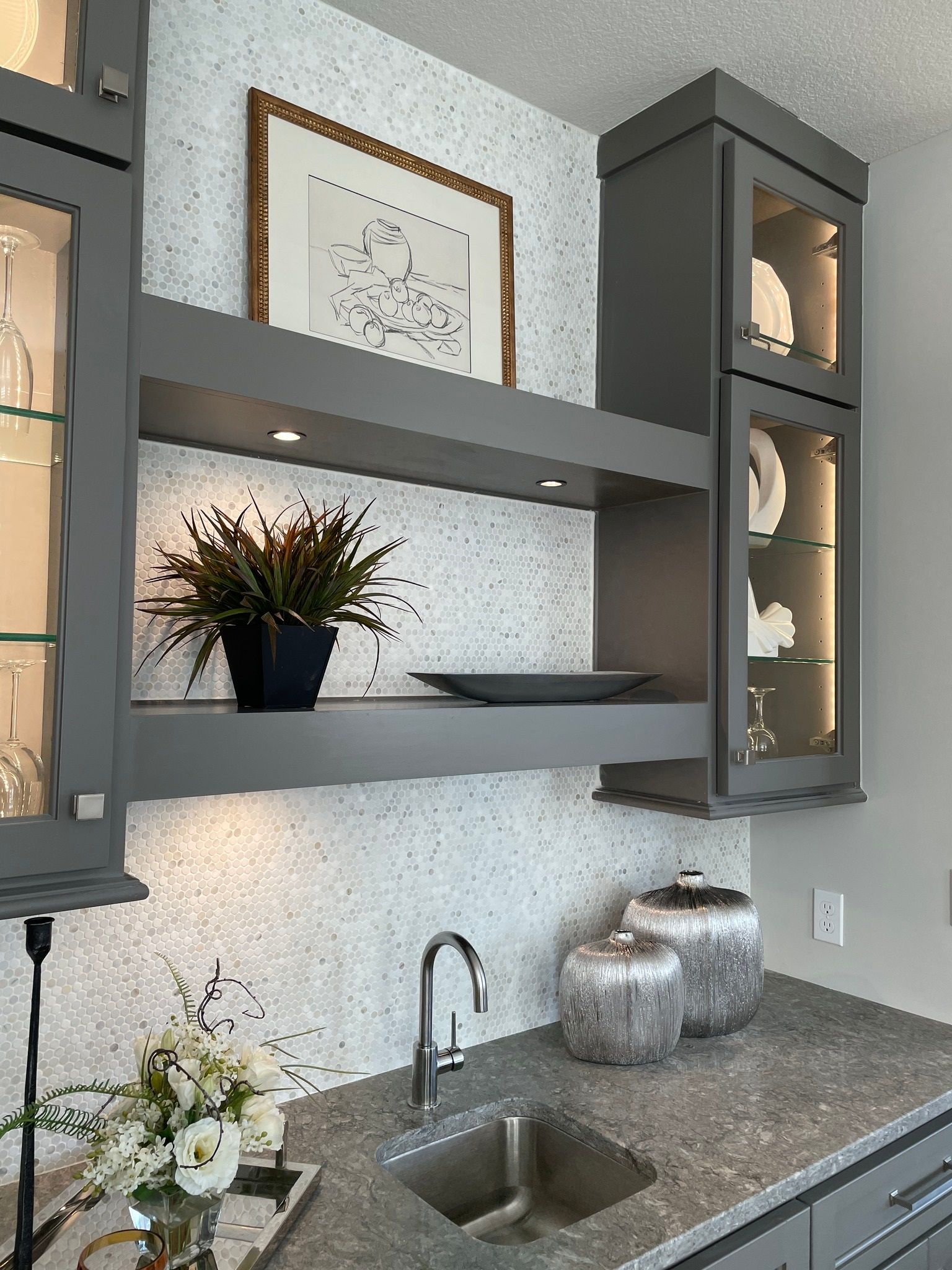 A kitchen with a sink , shelves , cabinets and a picture on the wall.
