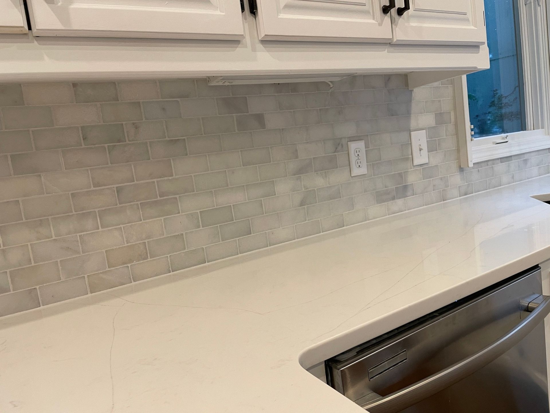 A kitchen with white cabinets , white counter tops , and a stainless steel dishwasher.