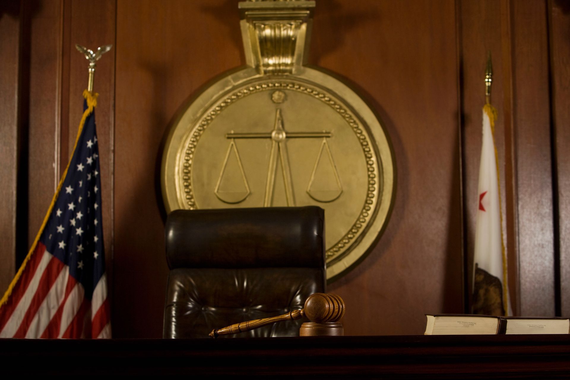 Judge’s bench with a gavel, gold scales emblem, and U.S. and state flags in a courtroom