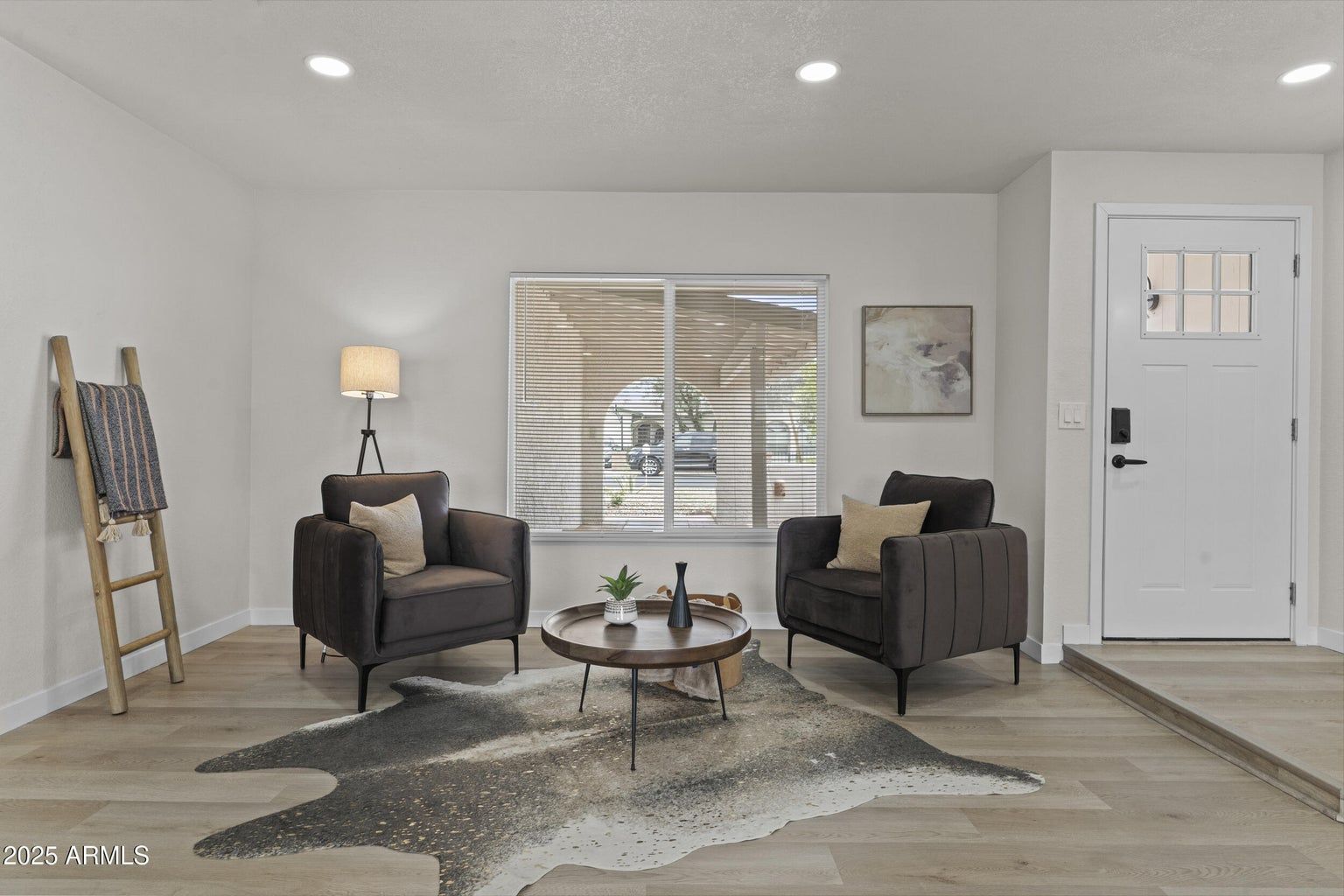 Bright living room with two dark armchairs, round coffee table, rug, lamp, and front door.