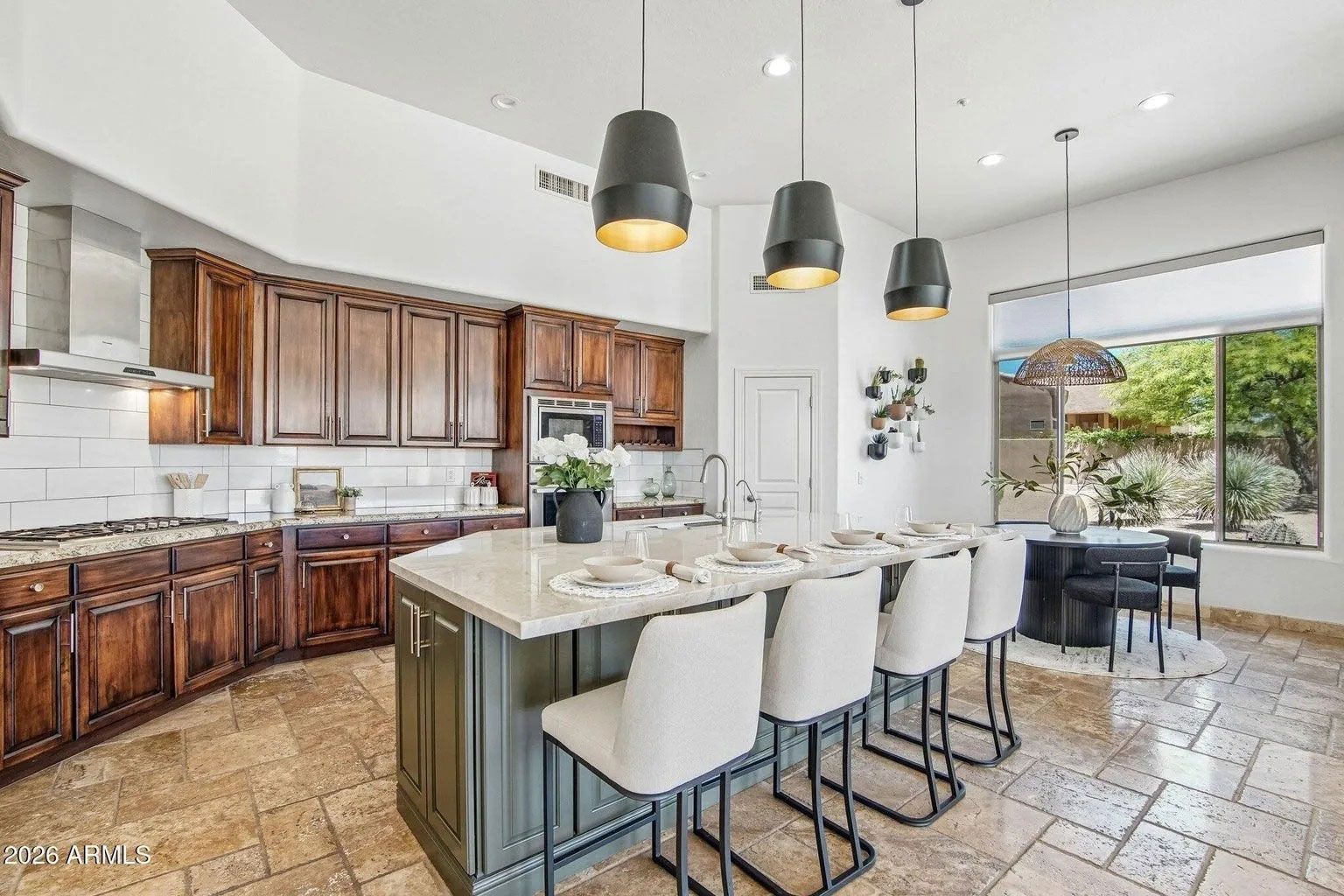 Bright modern kitchen with wood cabinets, marble island, pendant lights, and barstools.