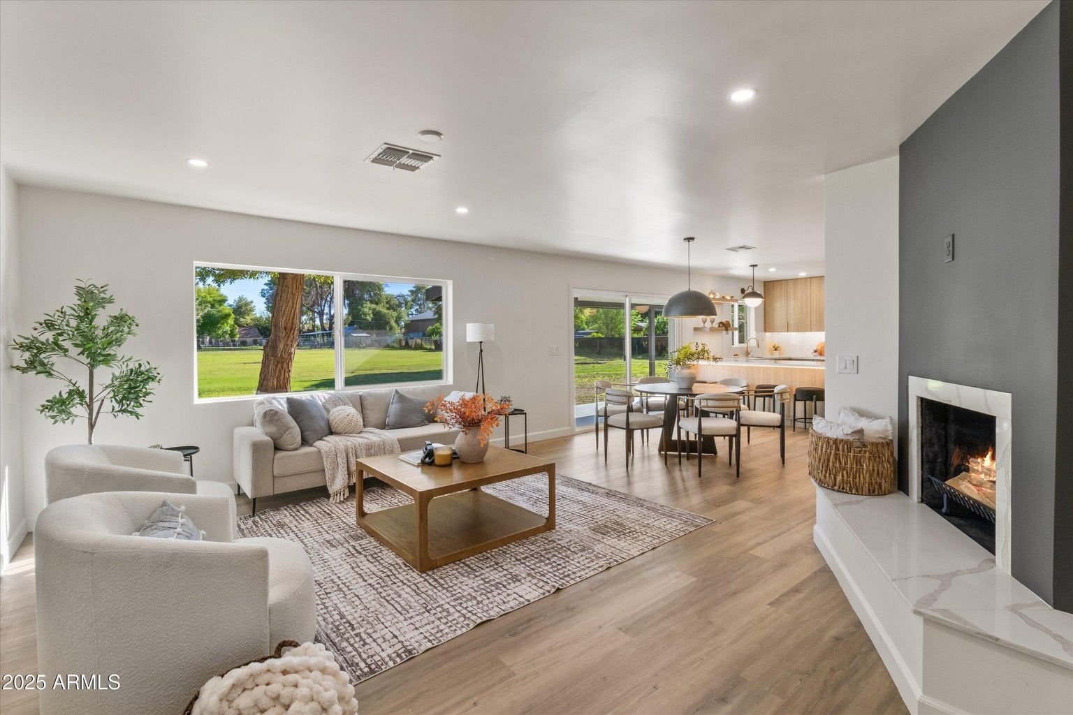Bright modern living room with gray sofas, fireplace, large windows, and open dining area.