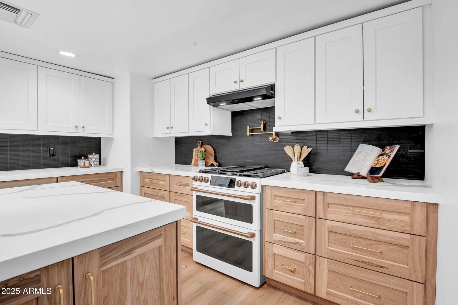 Bright modern kitchen with white cabinets, wood lower cabinets, black backsplash, and stainless steel stove.