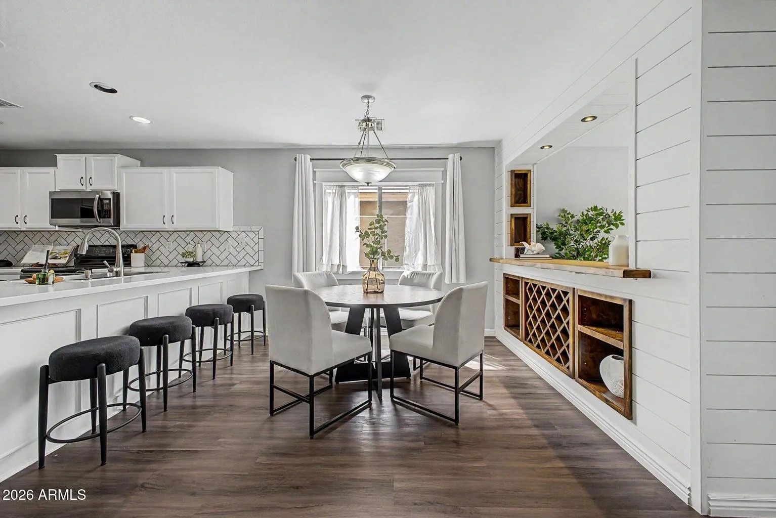 Bright open dining room and kitchen with white walls, dark wood floors, and a table with upholstered chairs.