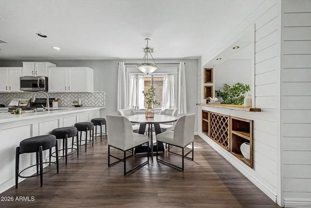 Bright open-concept kitchen and dining room with white cabinets, gray chairs, dark floors, and a long island