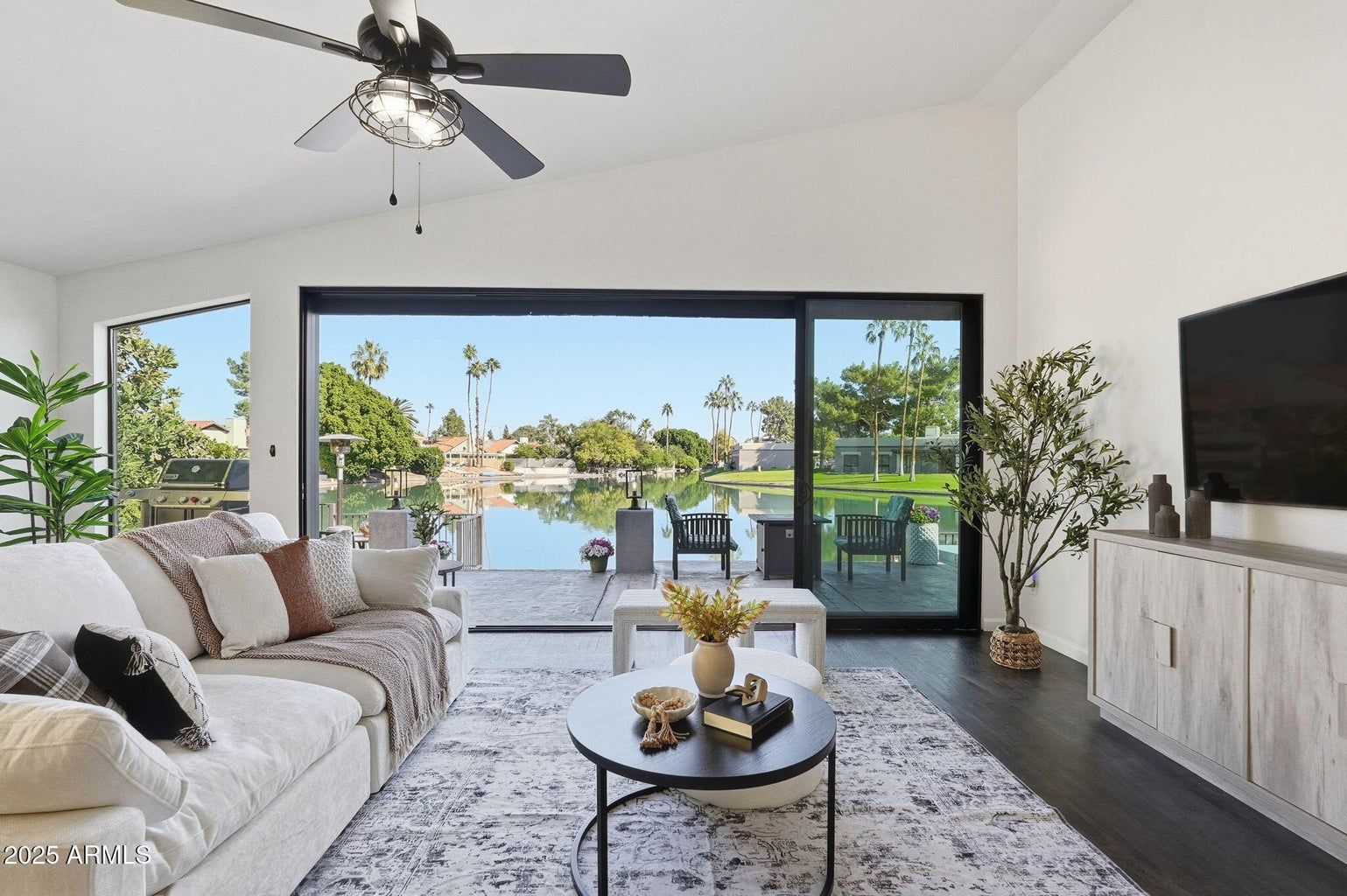 Bright living room with sofa, coffee table, TV, and open view to a waterfront patio.