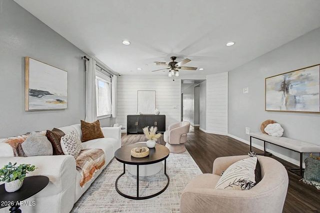 Bright modern living room with white sofa, beige chair, coffee table, fireplace, and large windows.
