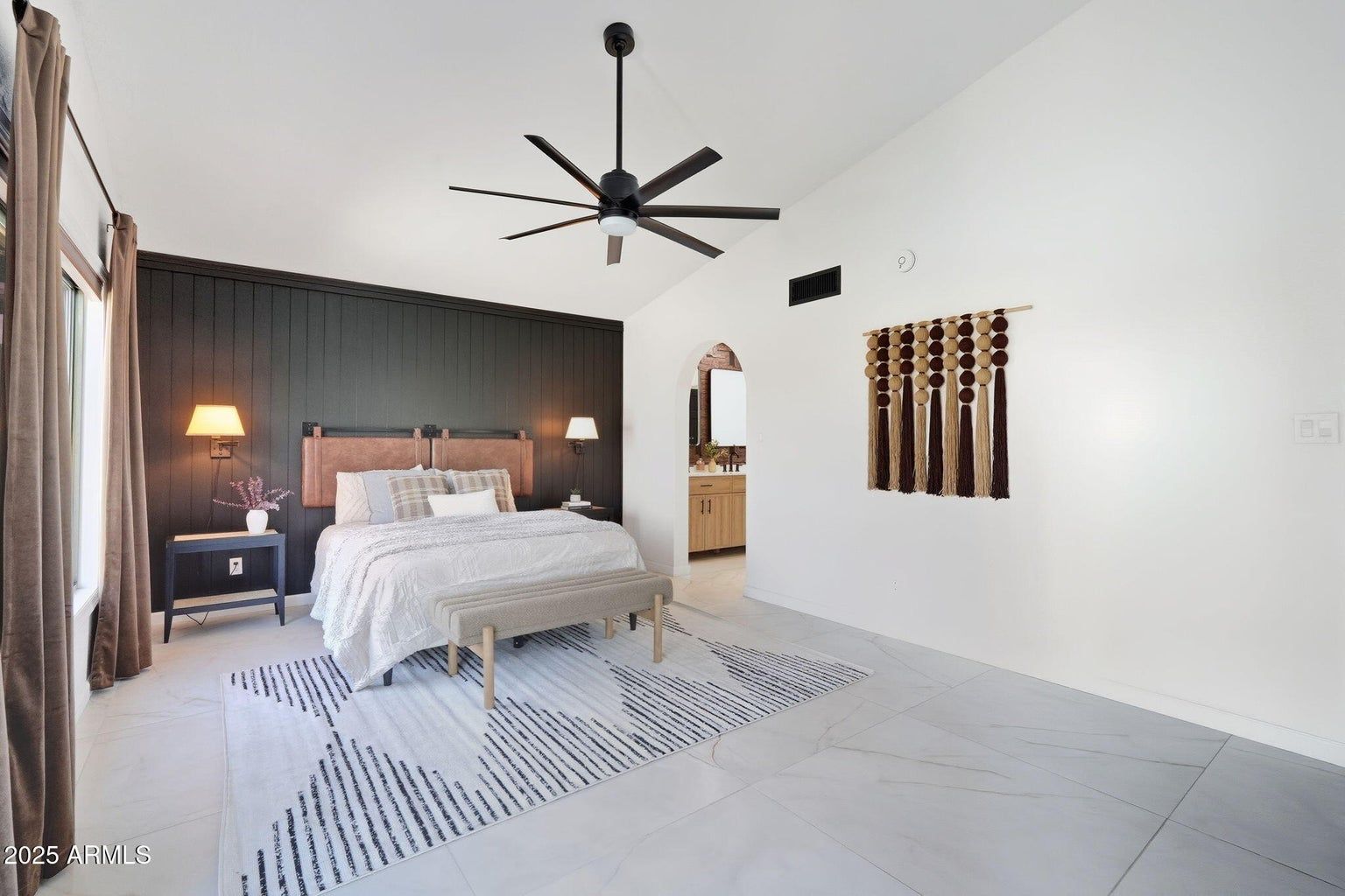 Modern white bedroom with a black accent wall, king bed, ceiling fan, and patterned rug.