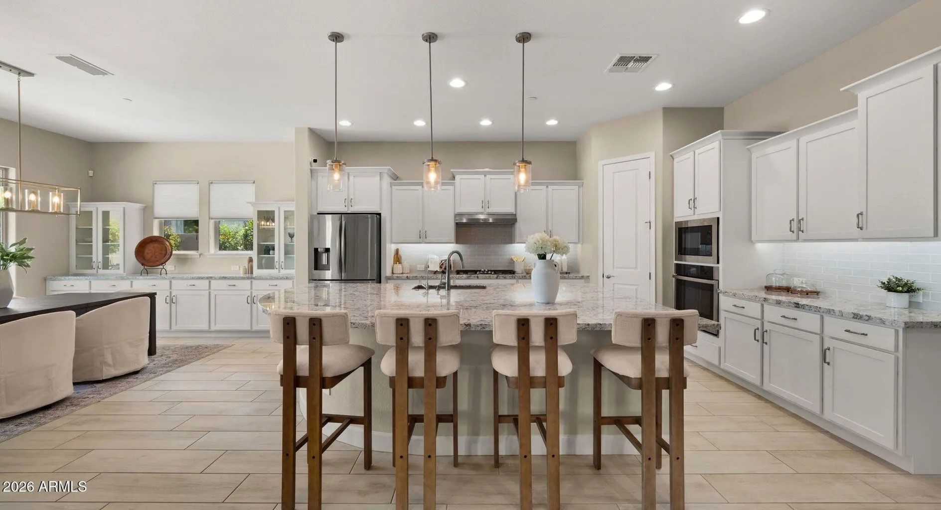 Bright modern kitchen with white cabinets, island stools, pendant lights, and open living area.