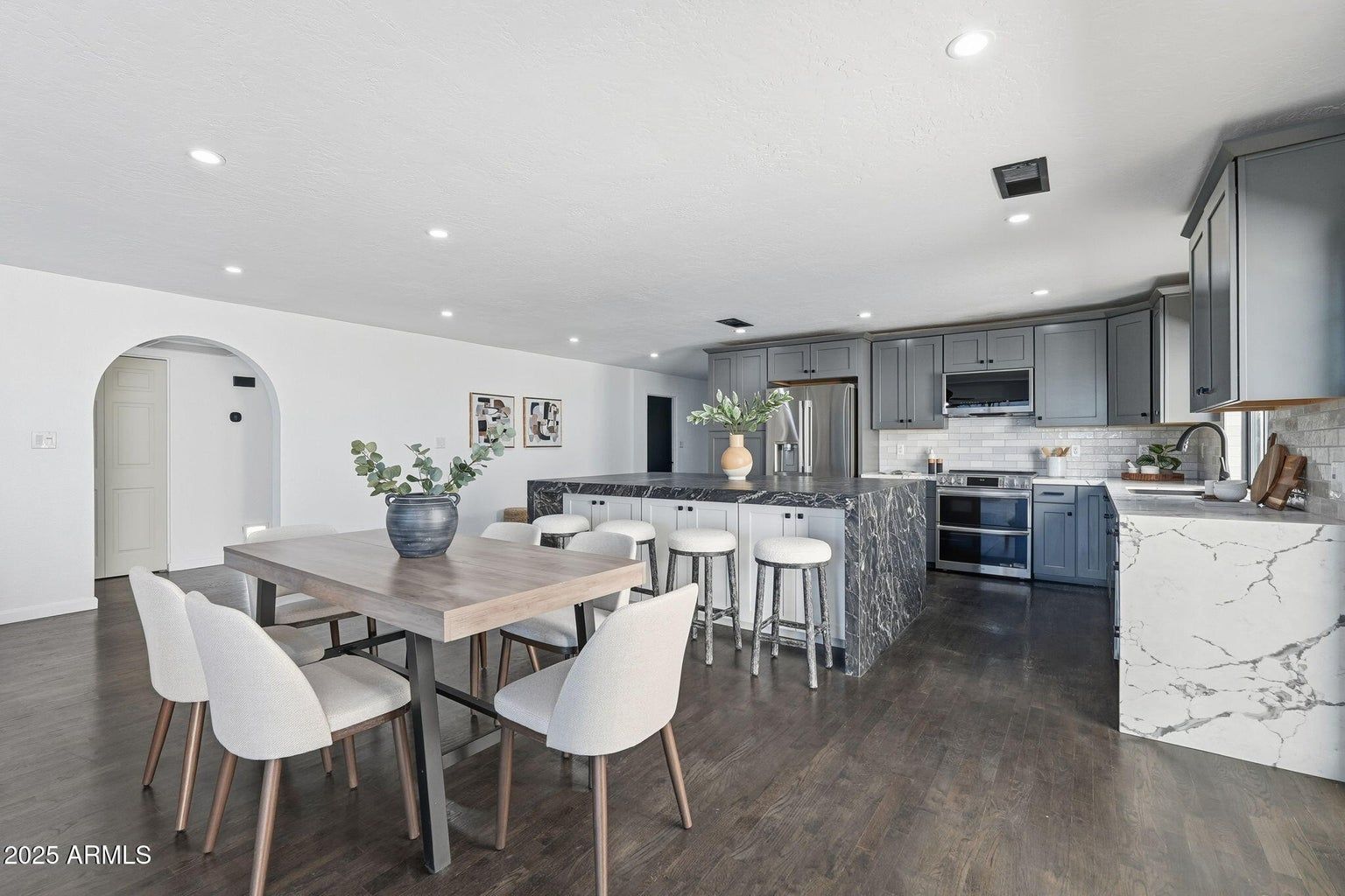 Modern open-concept kitchen and dining area with gray cabinets, dark floors, and white chairs around a table.