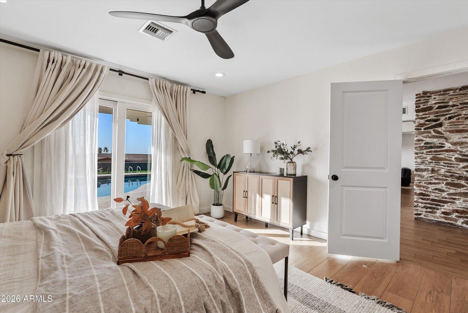 Bright bedroom with a bed, beige curtains, ceiling fan, and open door to a hallway.