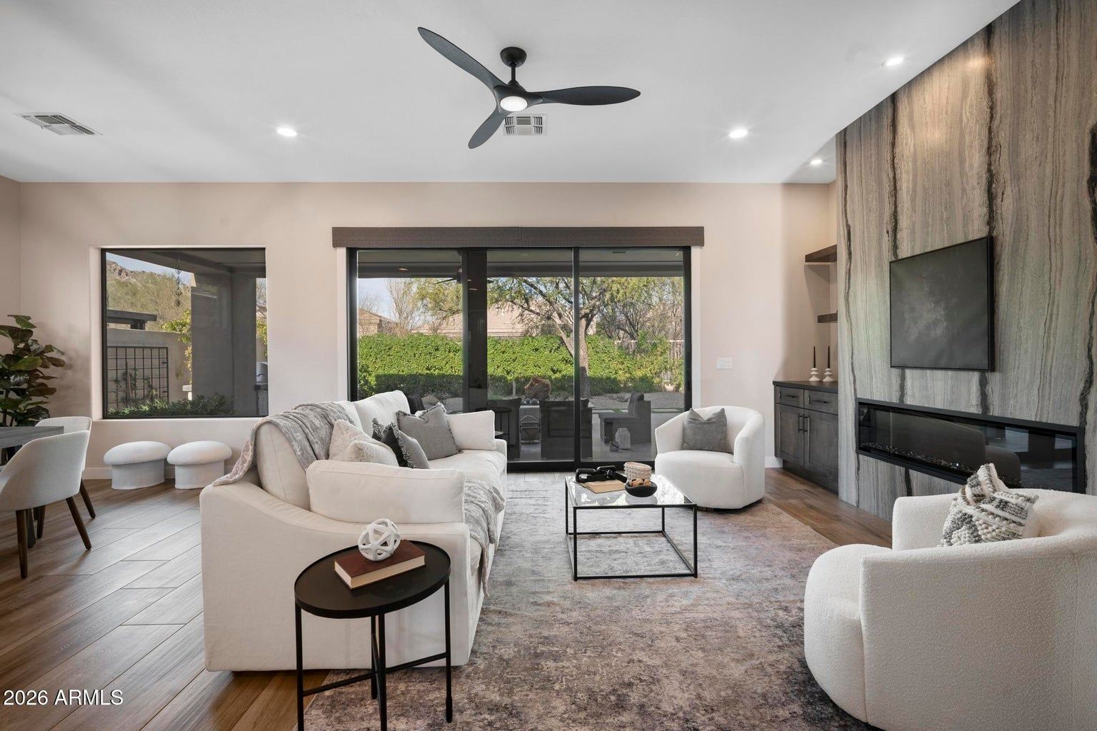 Bright modern living room with white sofas, fireplace, large windows, and sliding doors to a patio.