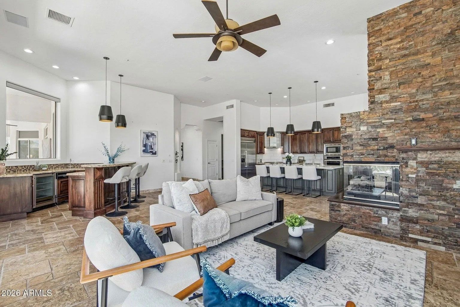 Open-concept living room with brick fireplace, sectional sofa, and kitchen island in the background.