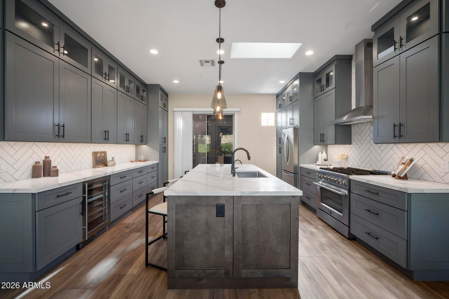 Modern gray kitchen with a large island, dark cabinets, and white countertops in bright natural light.