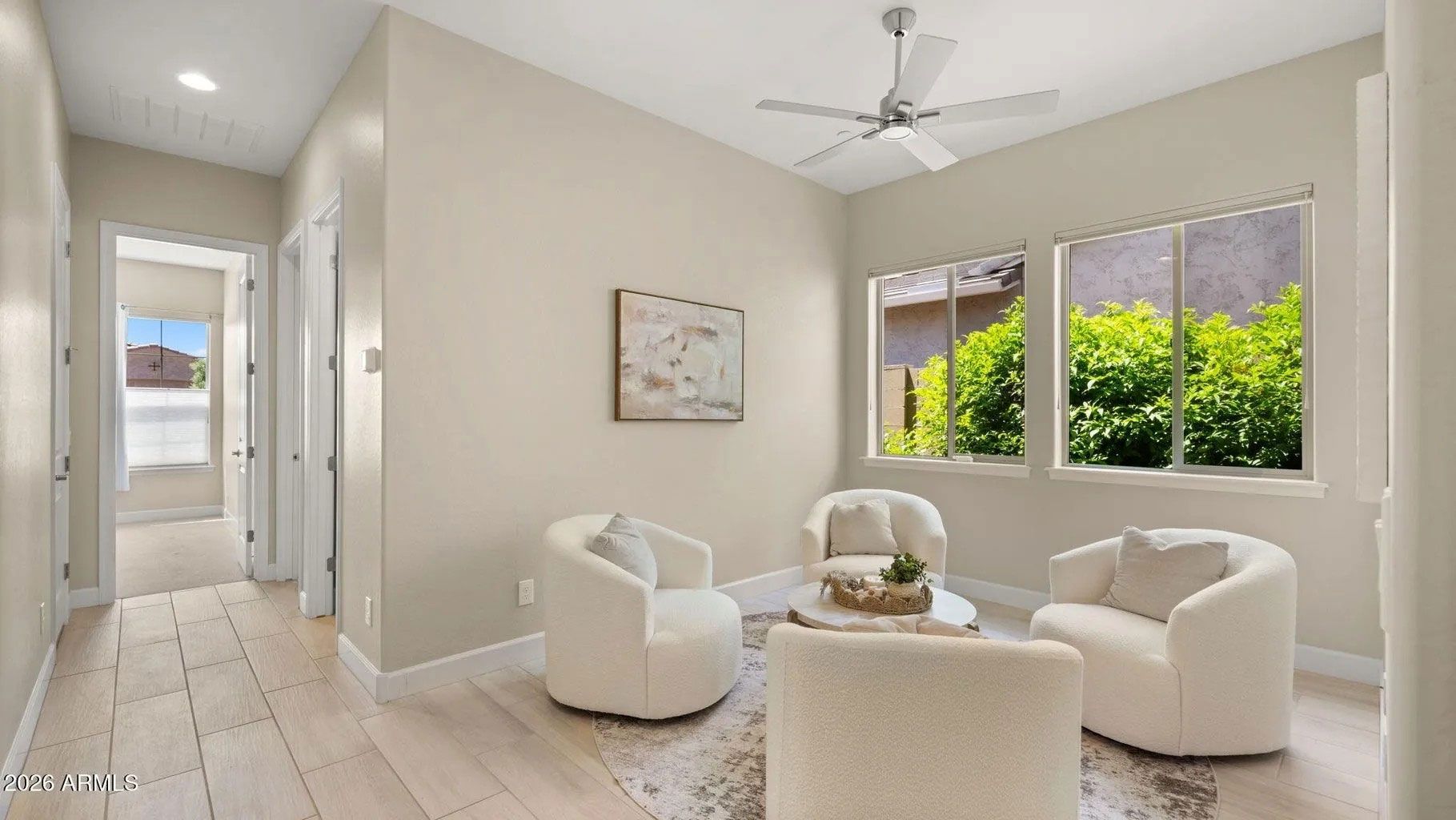 Bright living room with white chairs, coffee table, and large windows overlooking greenery.