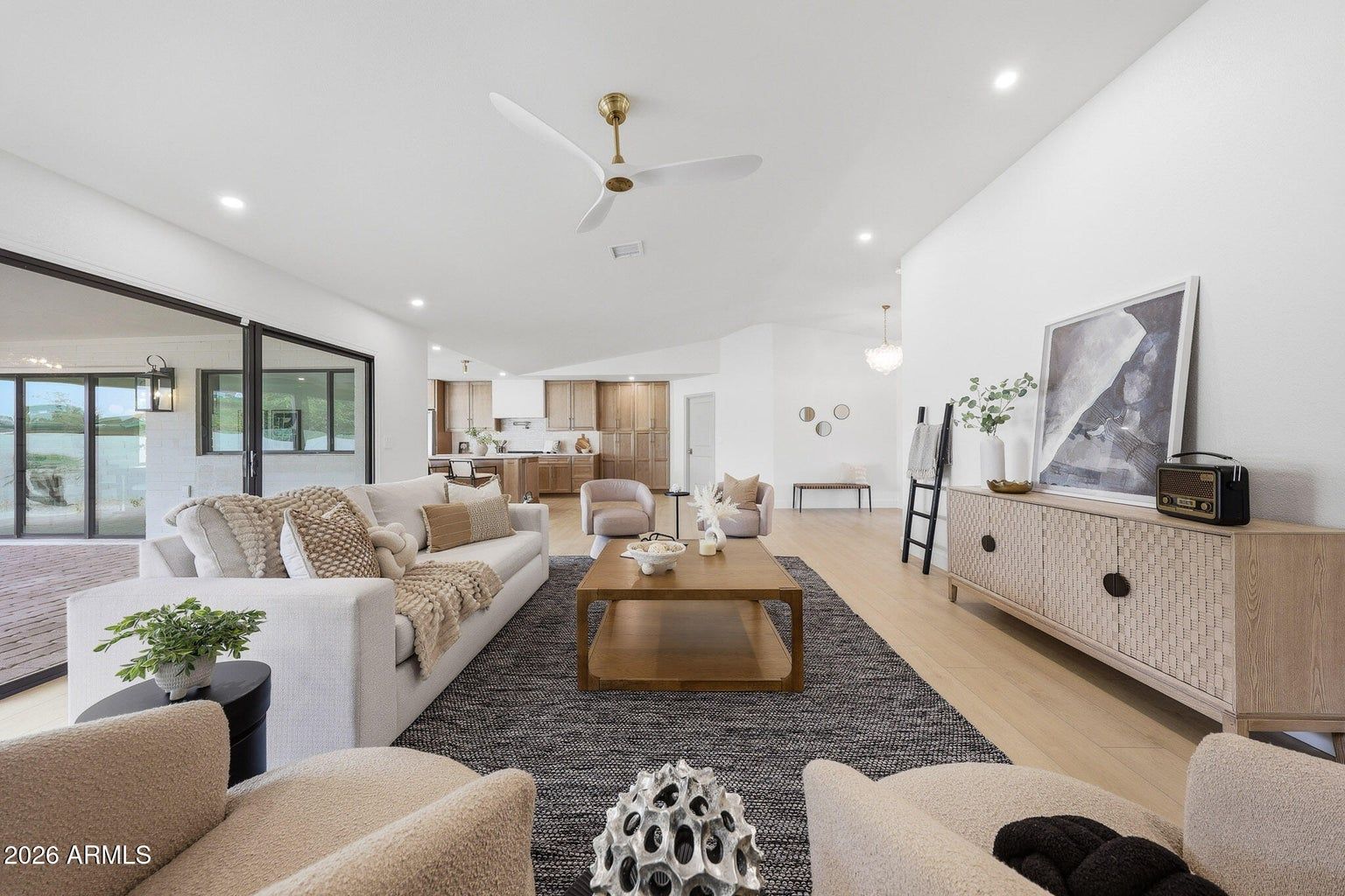 Bright modern living room with white sofas, patterned rug, wood console, and large windows.