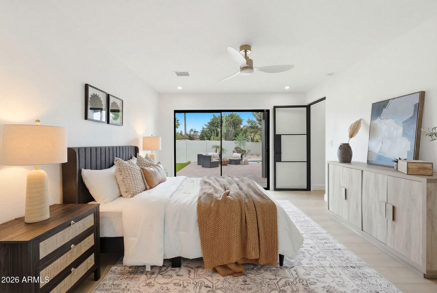 Bright bedroom with a bed, dresser, and large sliding doors opening to a patio and ocean view.