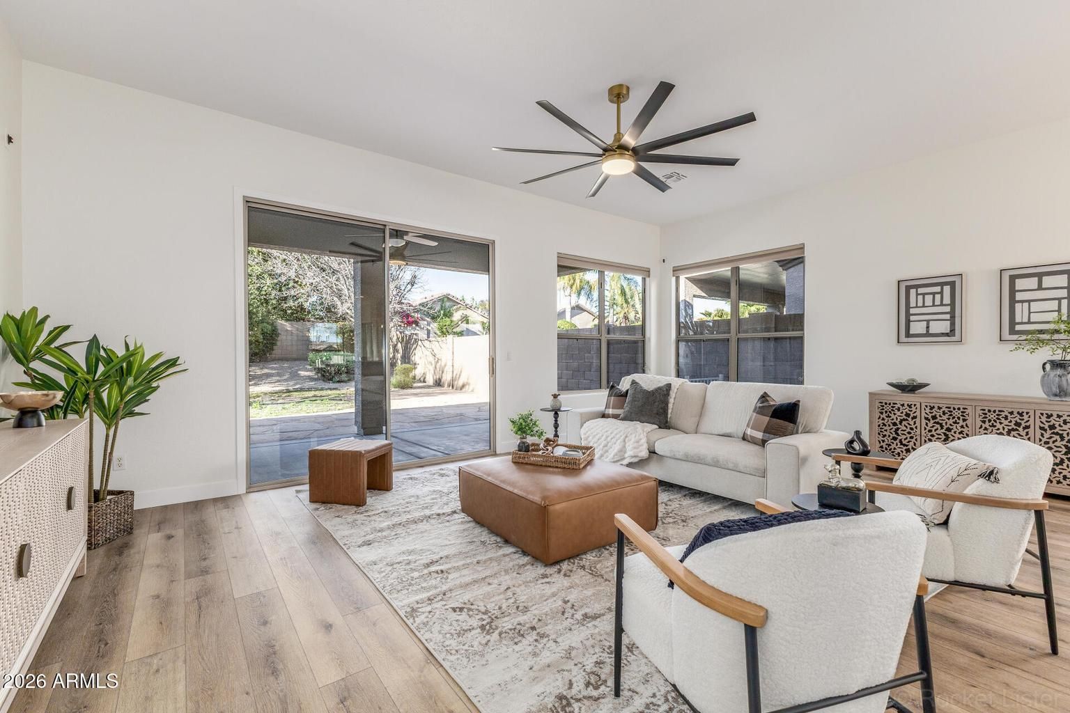 Bright modern living room with white sofa, wood floors, ceiling fan, and open sliding doors to a patio.