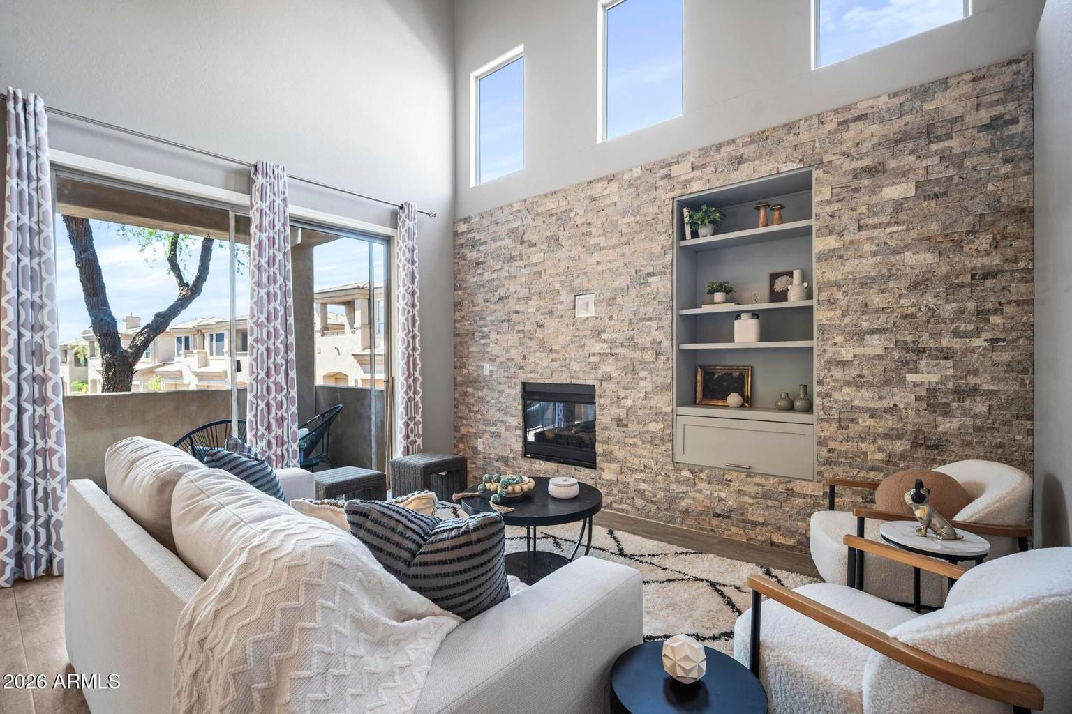 Bright modern living room with stone fireplace, tall windows, and beige sofas.