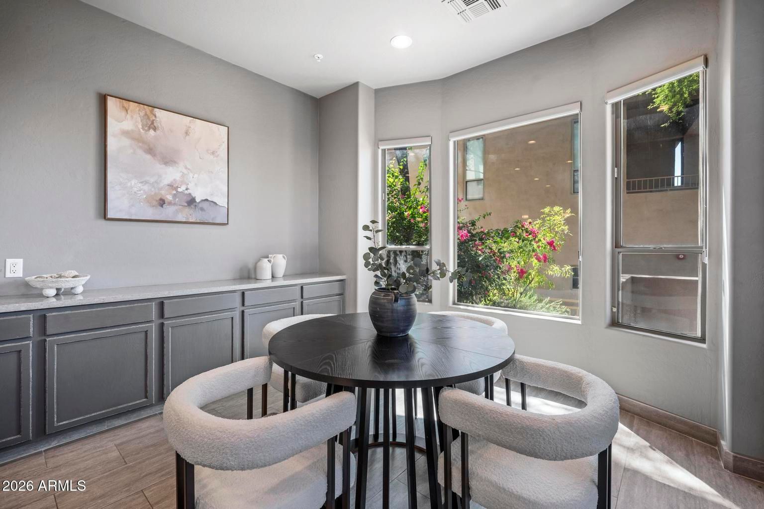Modern dining area with round black table, gray chairs, built-in cabinet, and large windows.