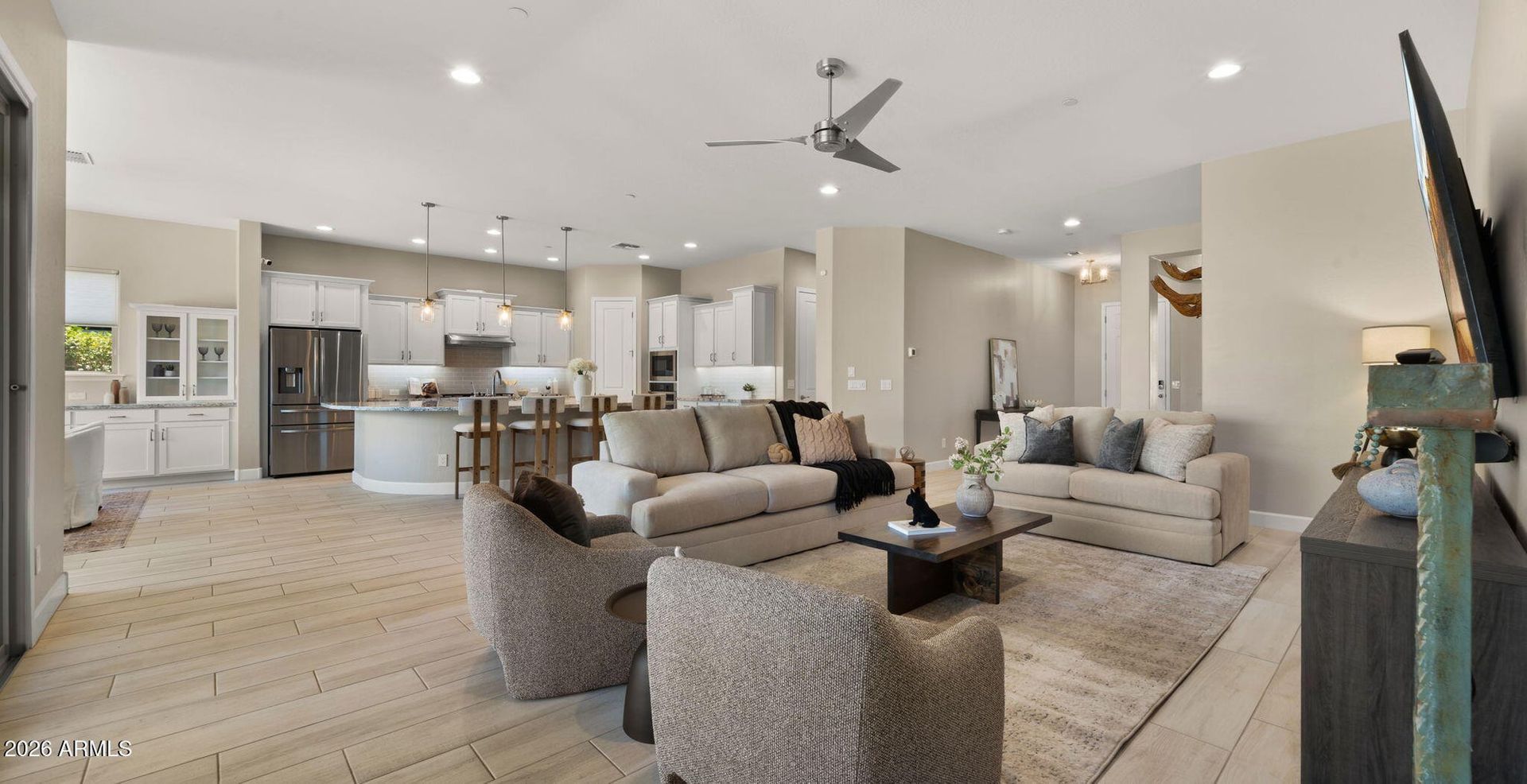 Spacious modern living room with sectional sofa, armchairs, TV, and open kitchen in neutral tones.