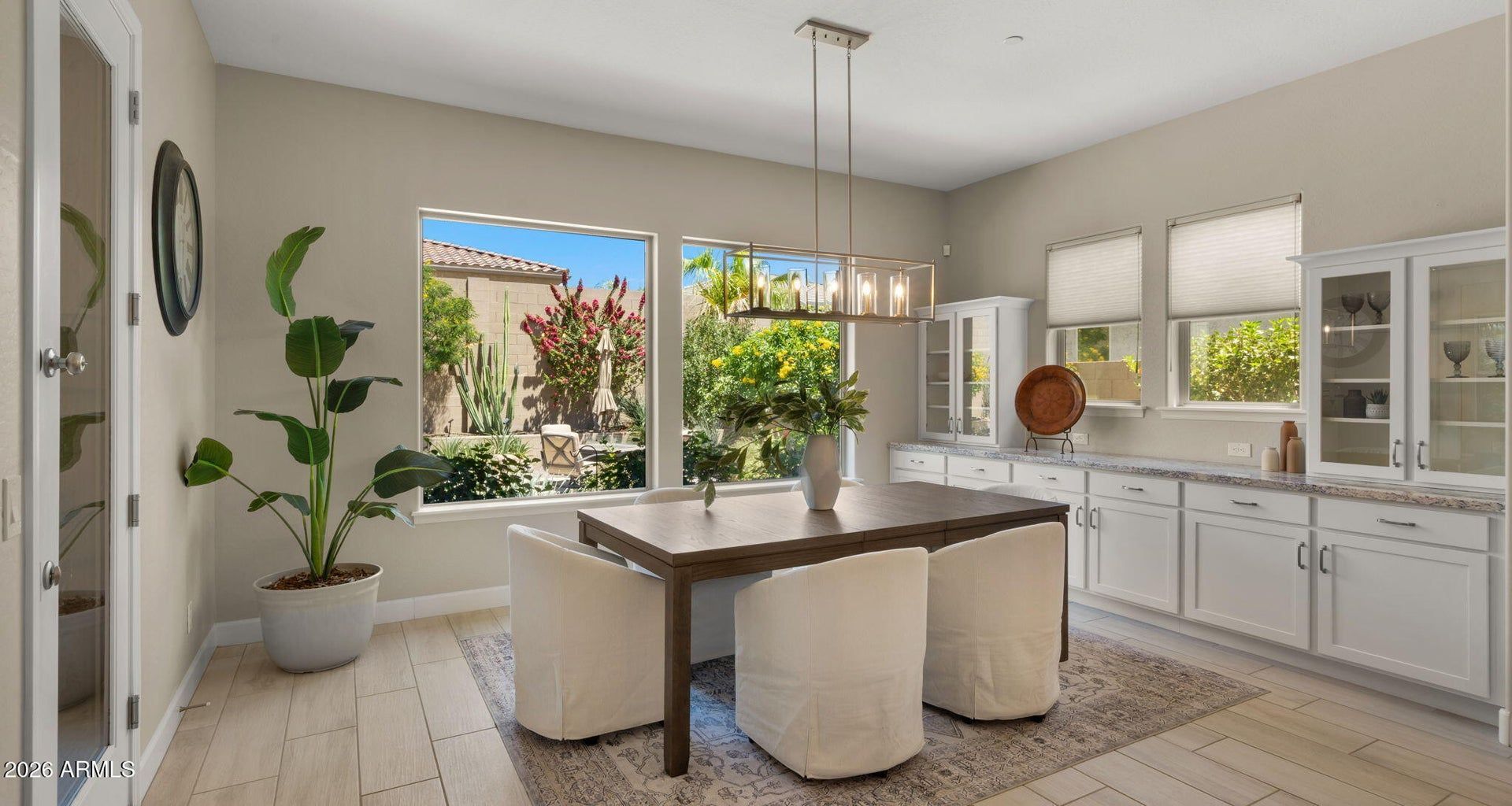 Bright modern kitchen with white cabinets, large island, pendant lights, and open windows overlooking greenery.
