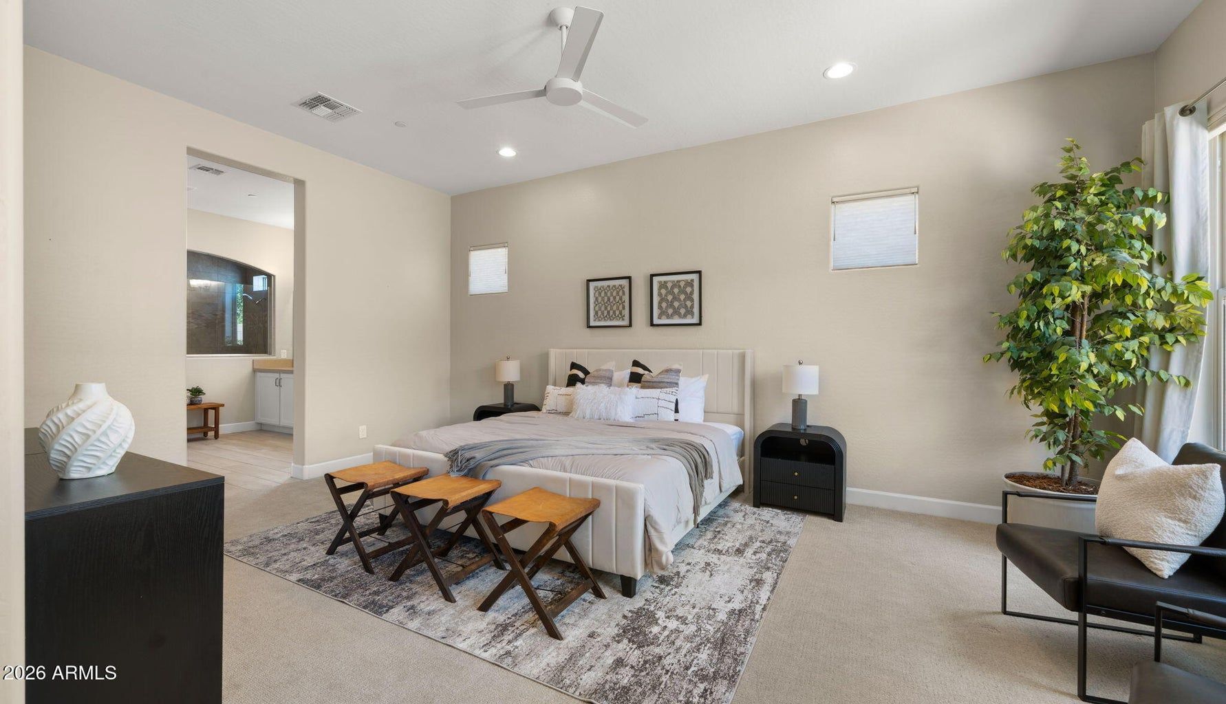 Bright bedroom with king bed, white bedding, gray accents, and a seating area beside large windows.