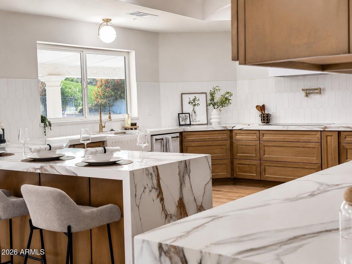 Modern kitchen with wood cabinets, marble island, and dining table near a bright window.