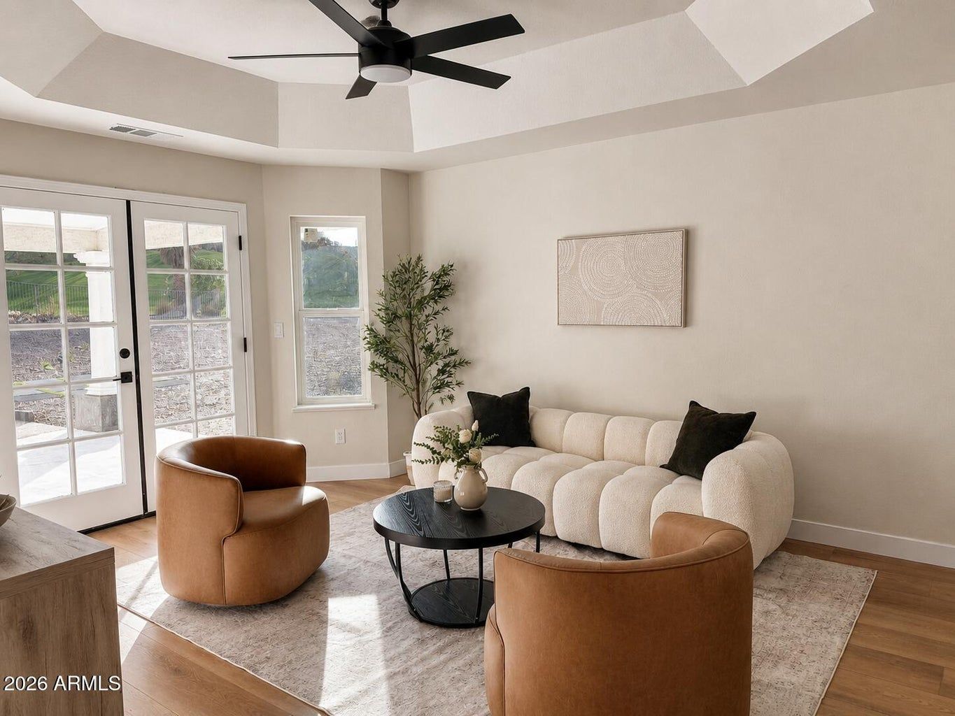 Bright living room with cream sofa, tan chairs, round coffee table, ceiling fan, and large windows.